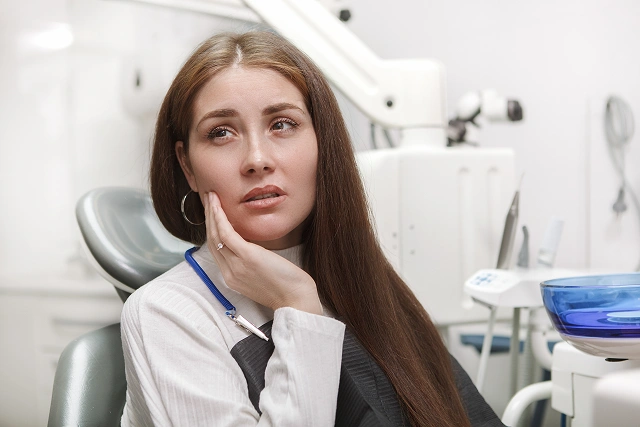 Female dentist in white coat thoughtfully posing in modern dental office setting.