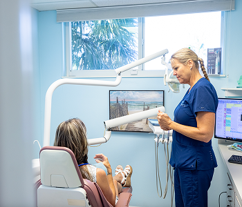 Pediatric dentist showing dental X-ray to young patient in modern dental office treatment room.